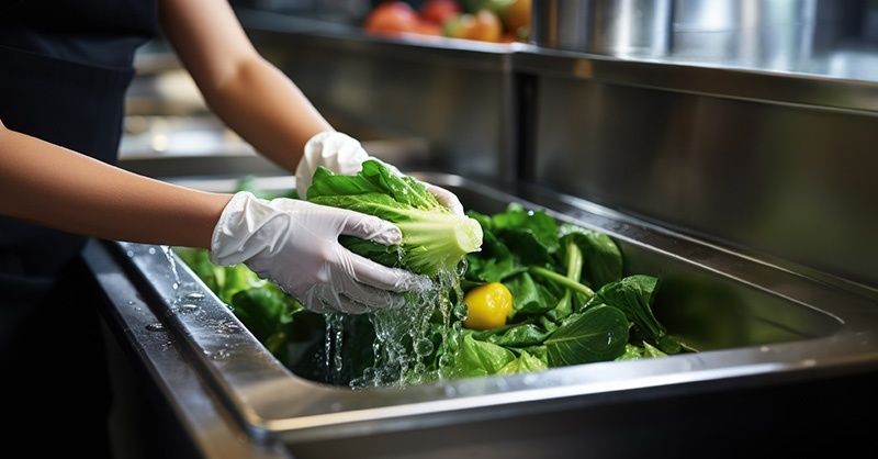 Keukenmedewerker wast groene groenten in een roestvrijstalen bak